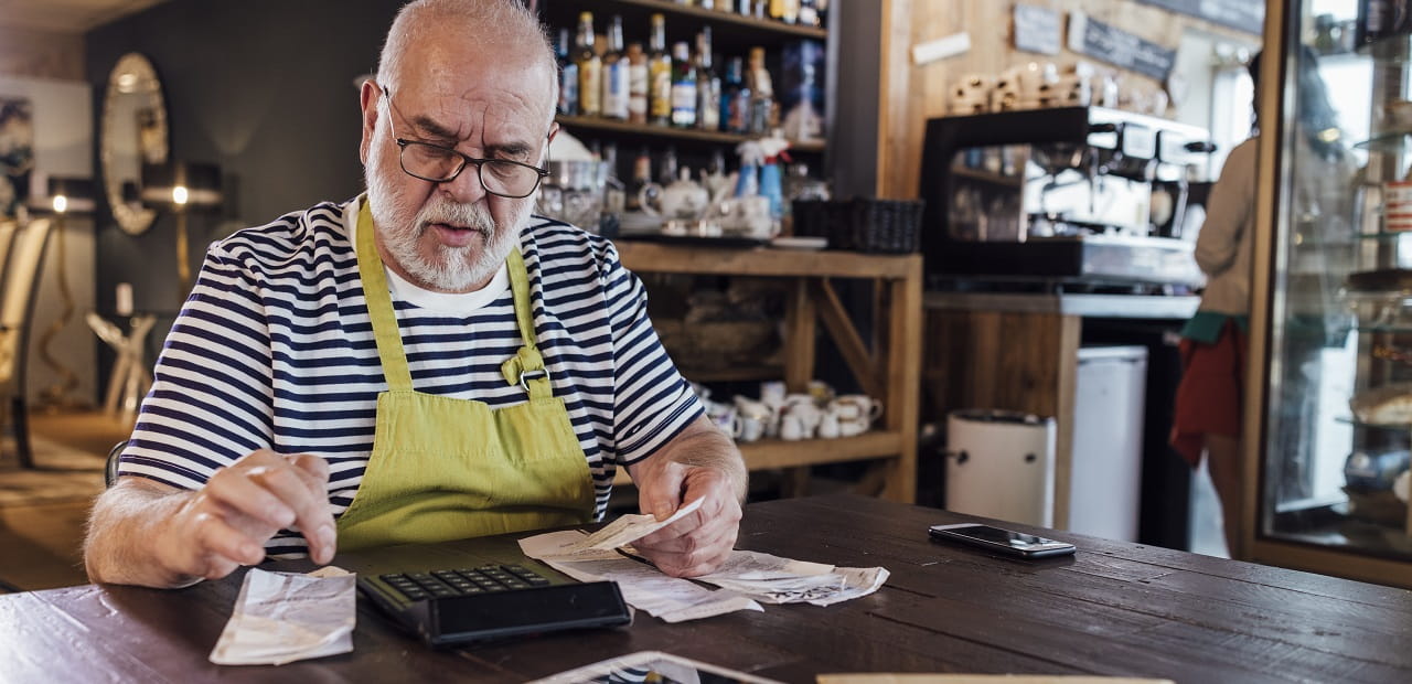 Man sits at a table in a workshop with receipts and a calculator.