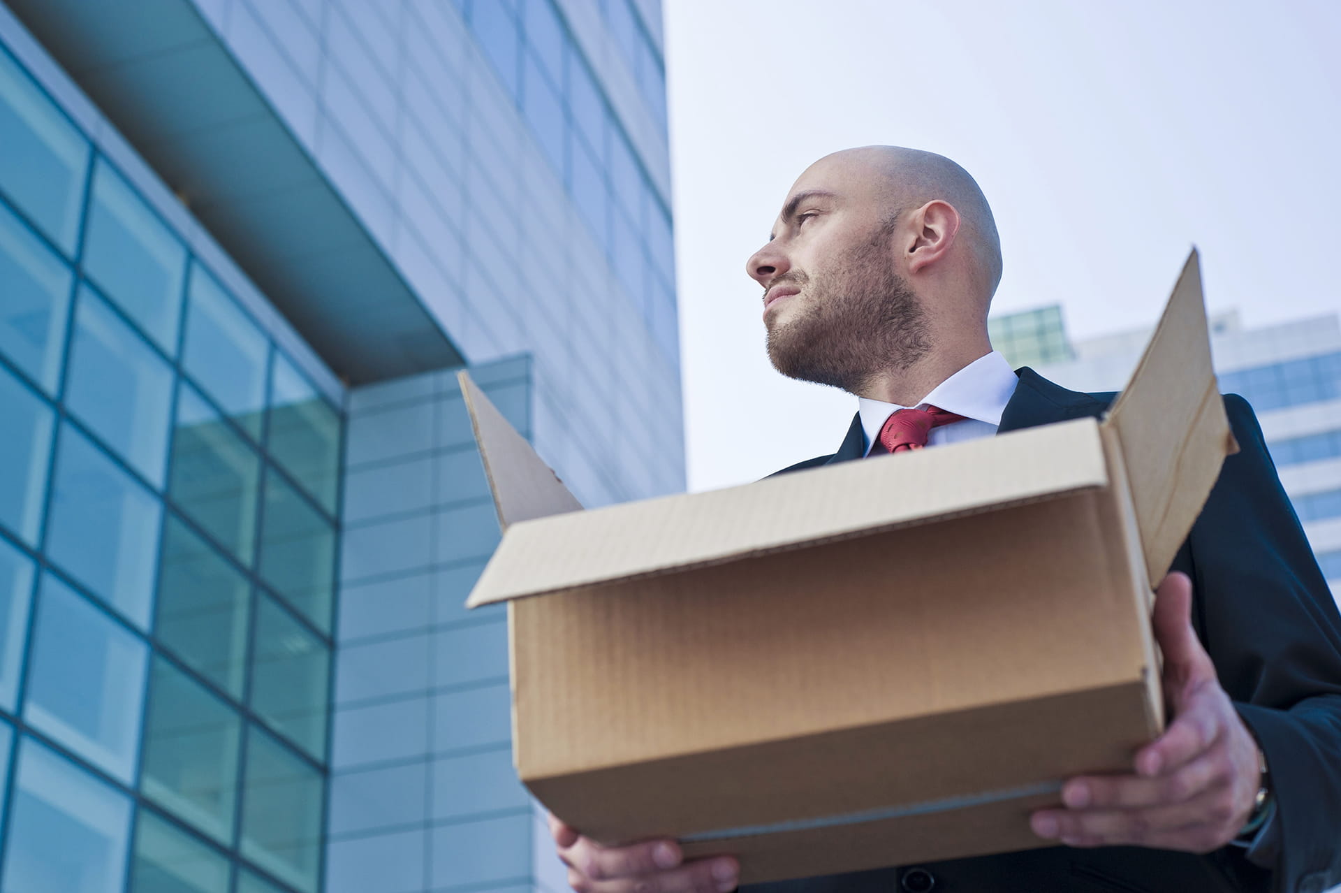 Young Businessman Holding A Cardboard Box Against Modern Skyscrapers