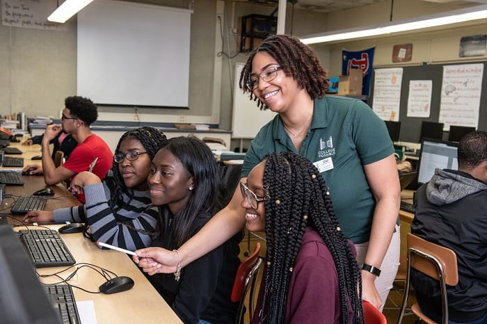 A smiling College Possible instructor with three high school girls in front of computers