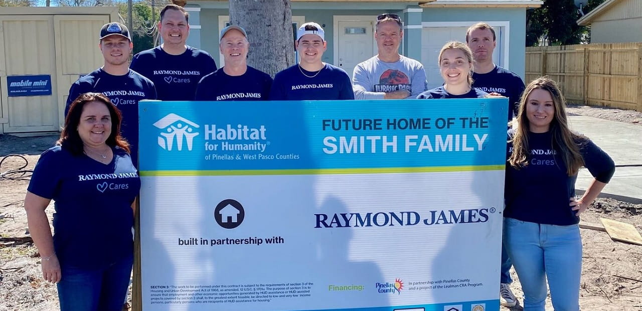 Raymond James volunteers pose behind sign that says "Future home of the Smith family"