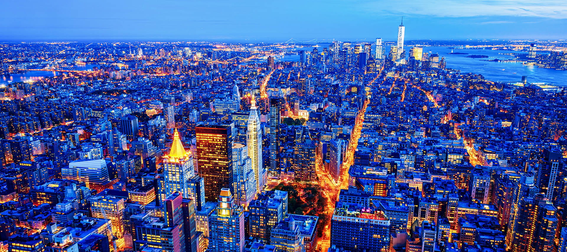 Illuminated Midtown and Lower Manhattan skyline at dusk.