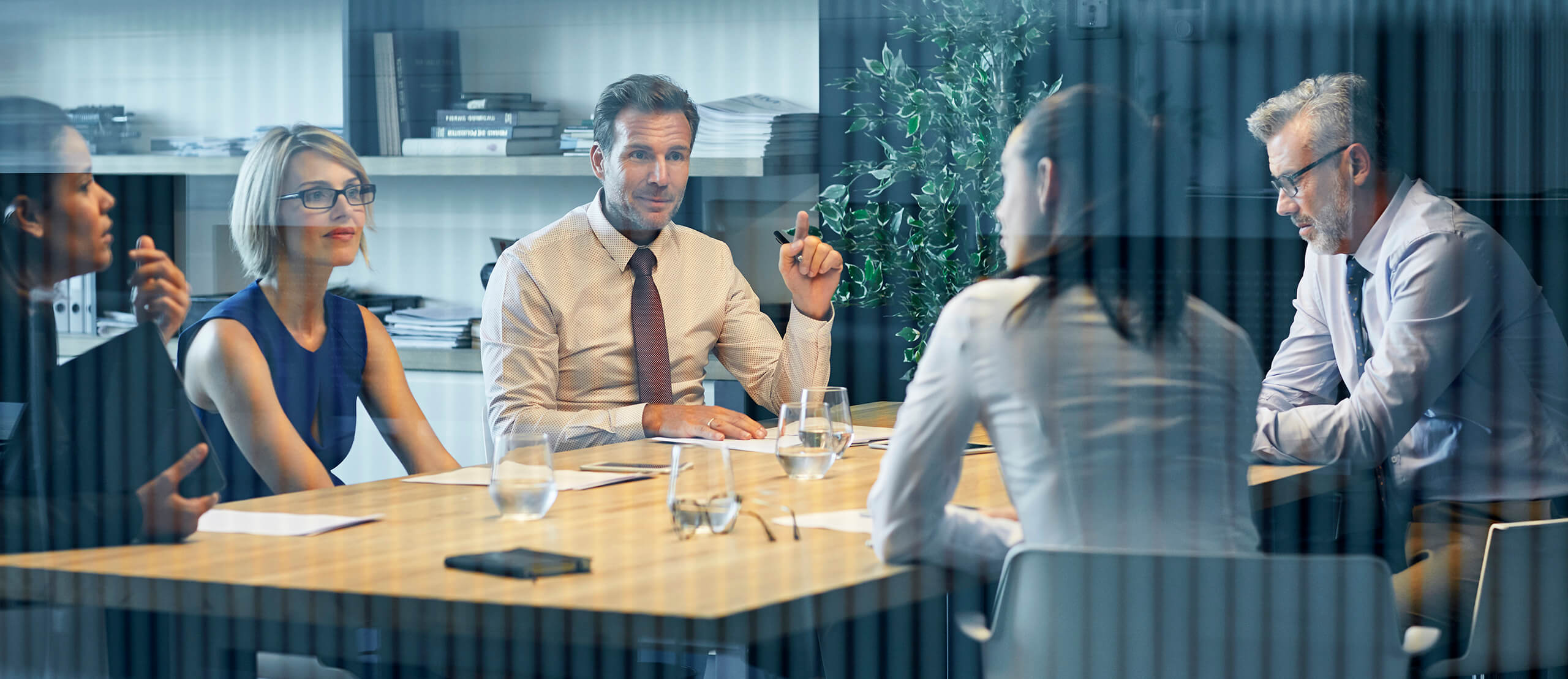 Business people communicating at desk seen through glass. Coworkers are discussing in meeting. They are sitting in office.