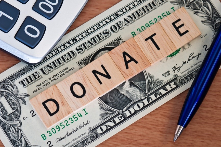The word "Donate" spelt using scrabble tiles on top of a dollar bill 