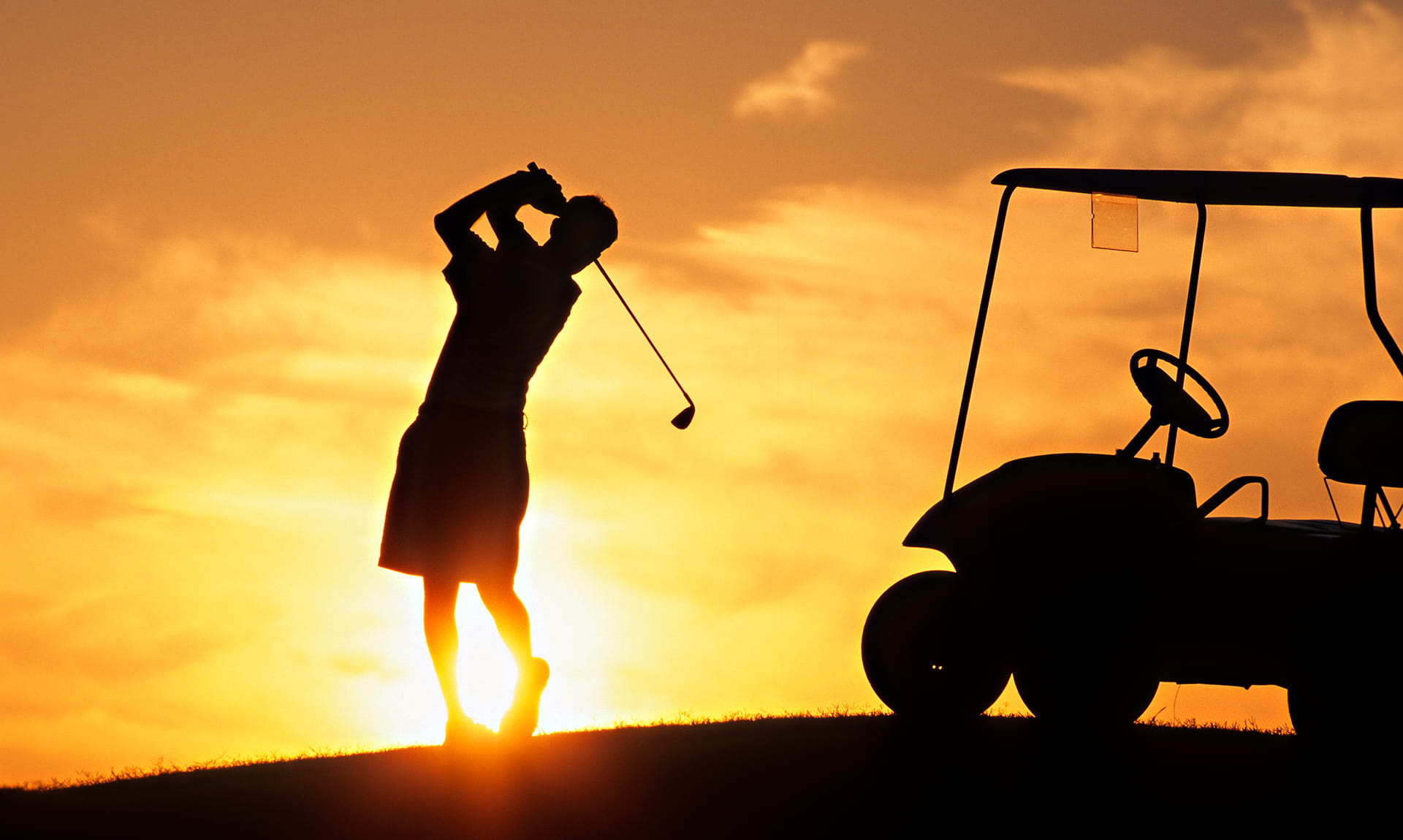 Man swinging golf club sunset