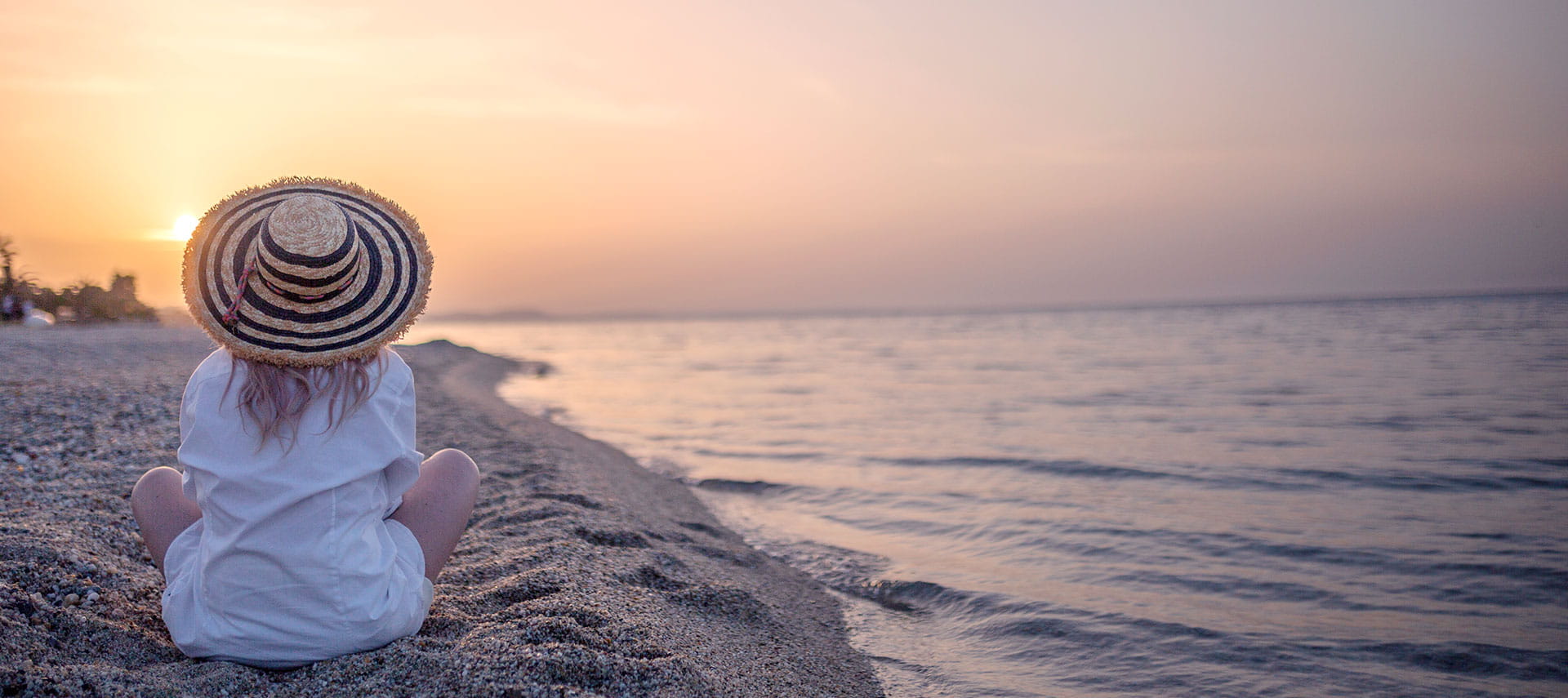 A women sitting down on the beach watching the sunset.
