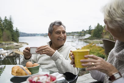 mature Caucasian couple drinking hot beverage next to lake