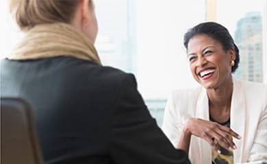 Black businesswoman smiling talking-to Caucasian businesswoman