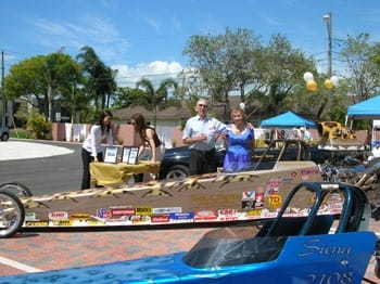 A group of people standing behind a brown soapbox racecar.