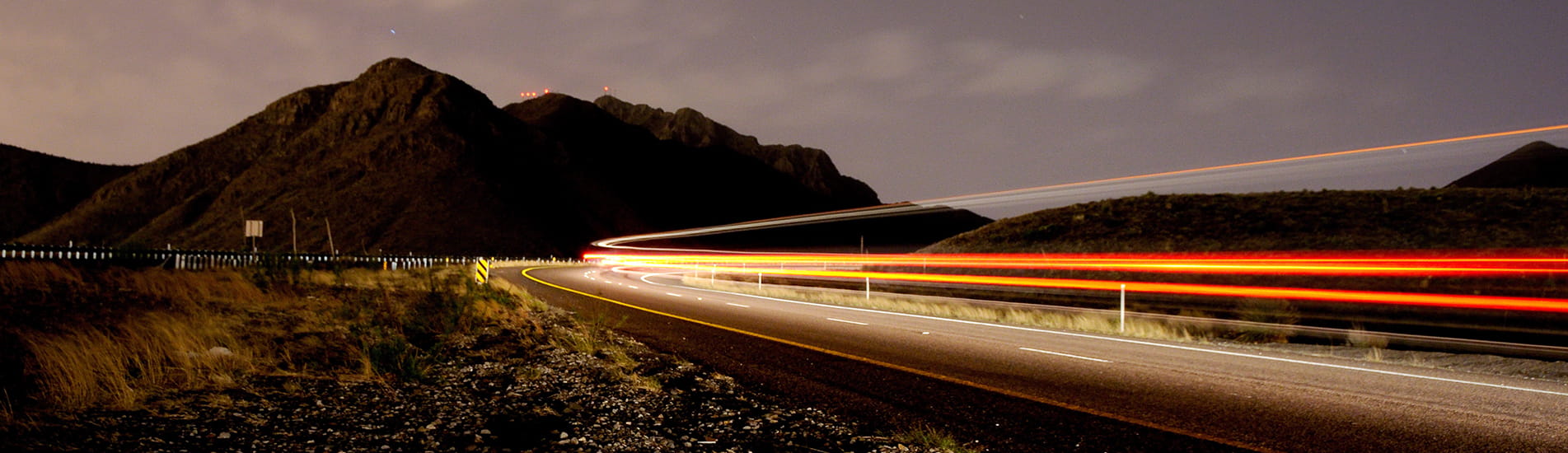 Highway at night with blurry lights and a mountain in the background.