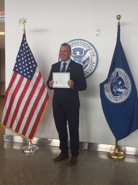Mick holding certificate and standing between flags