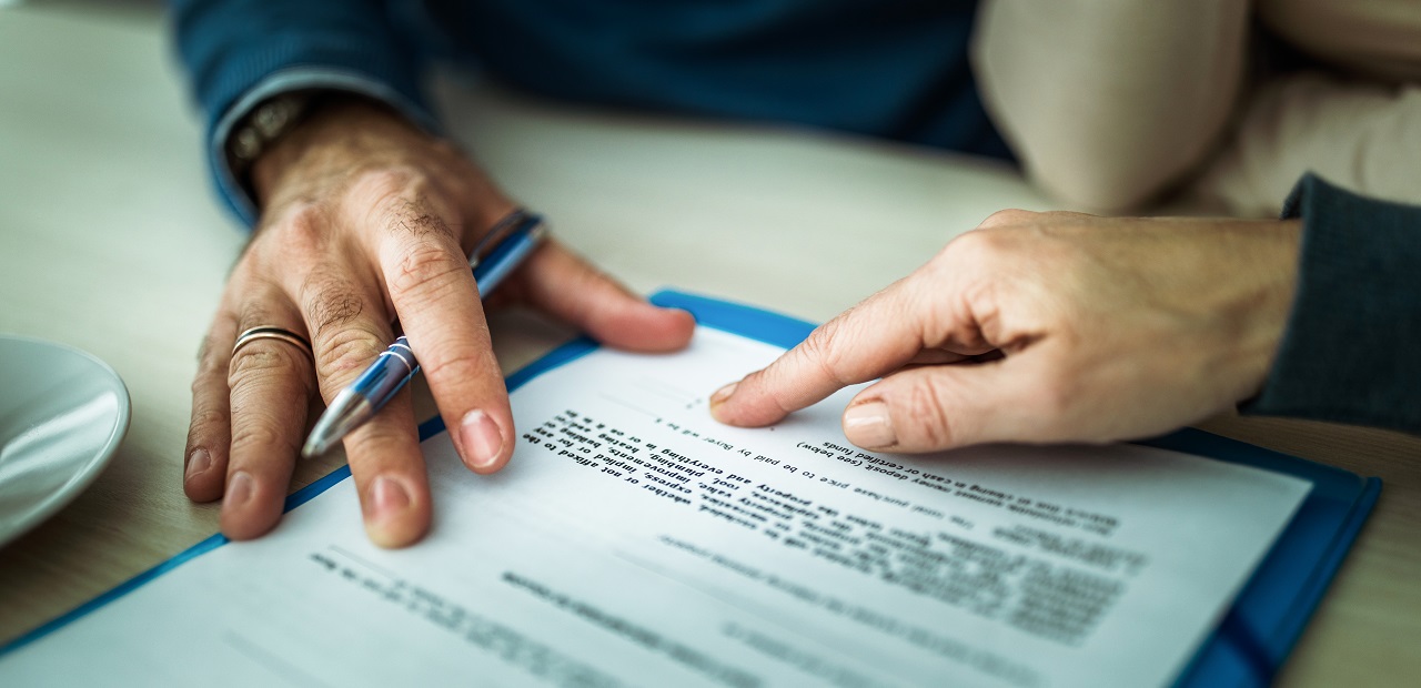 A close-up image of two people's hands pointing to the bottom of an official document.