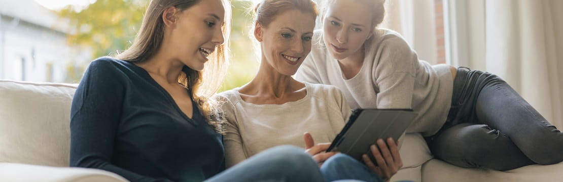 Mother and two daughters looking at tablet on a couch.