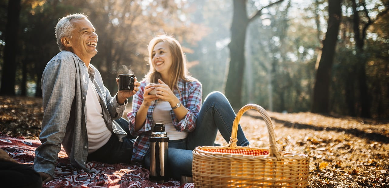 Man and woman sit outside sharing a hot beverage and smiling. 