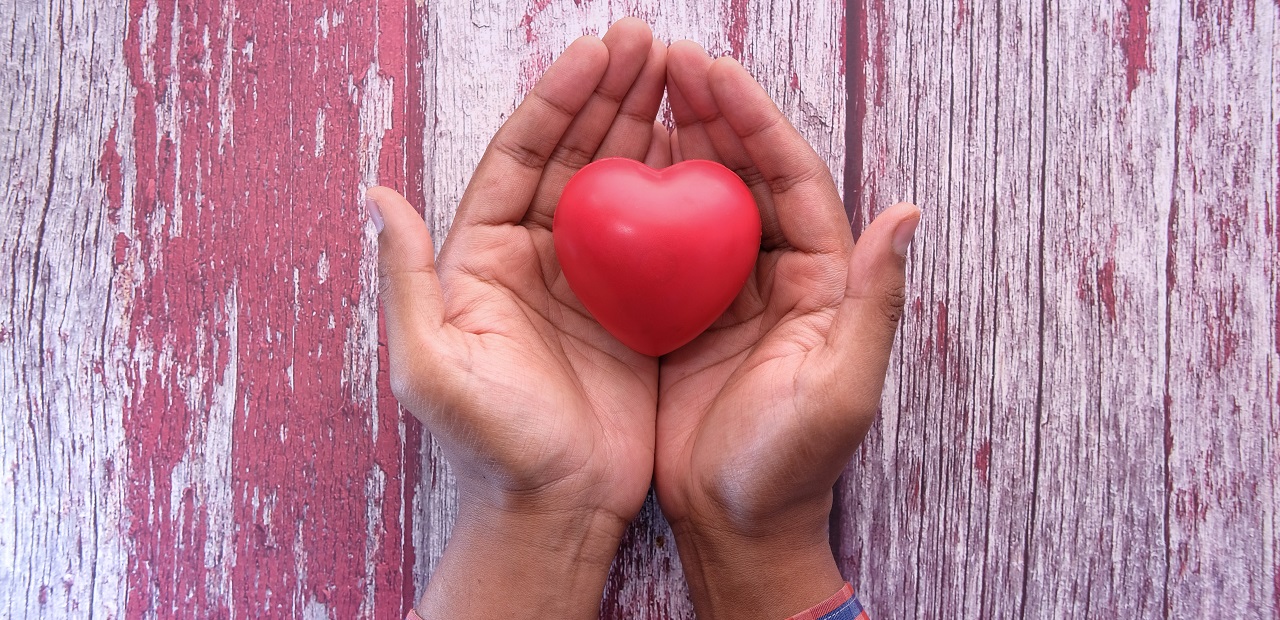 A close-up photo of two hands holding a red heart-shaped object