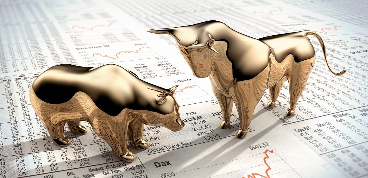 Metallic golden bull and bear figurines stand atop the financial section of a newspaper