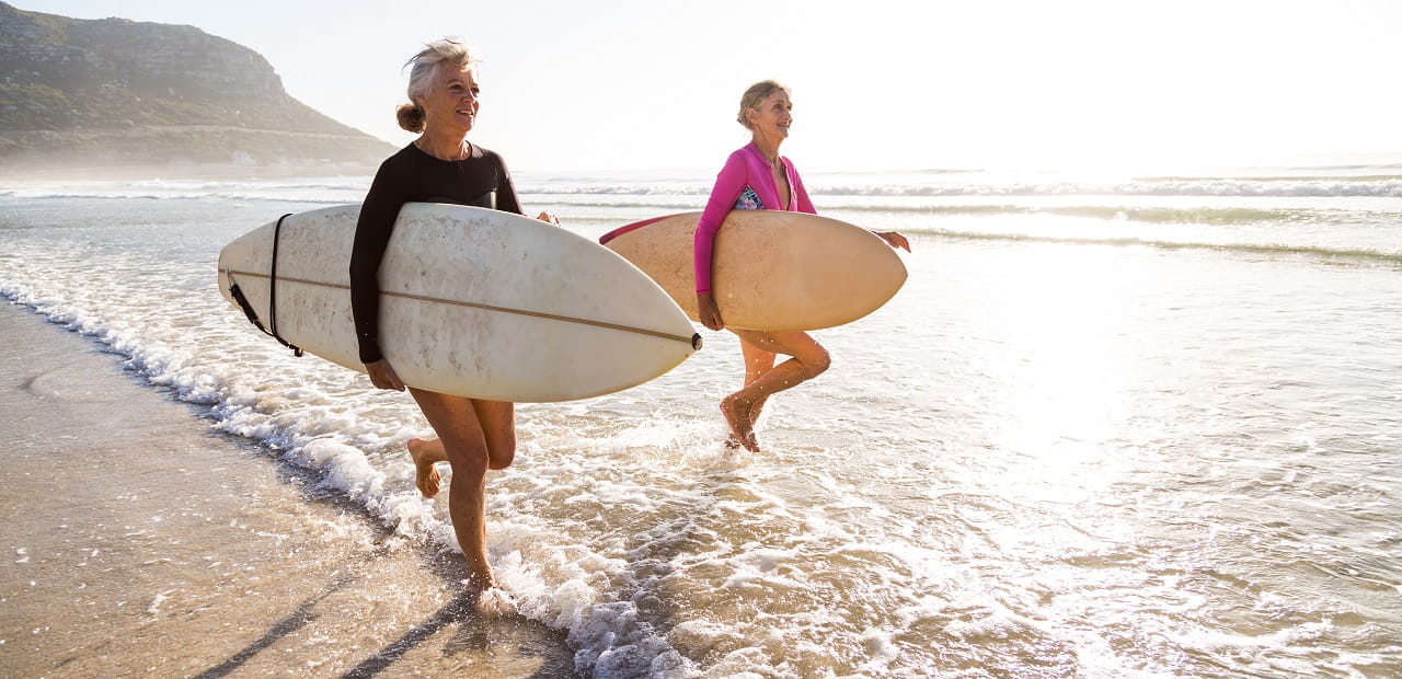 Two women run along the beach carrying surfboards