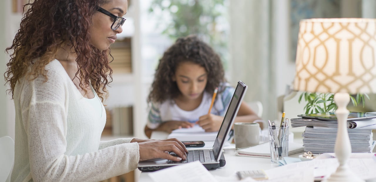 Woman and her daughter sit at a table together working. 