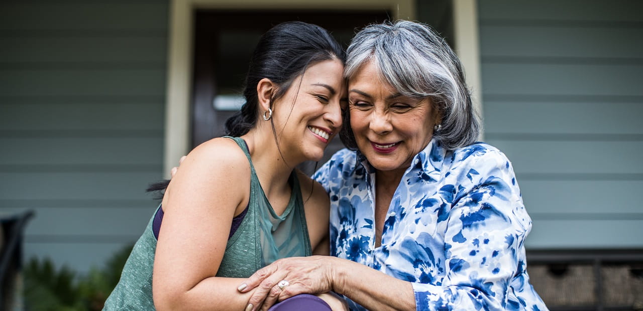 Two women sitting on a front porch step smiling and hugging.