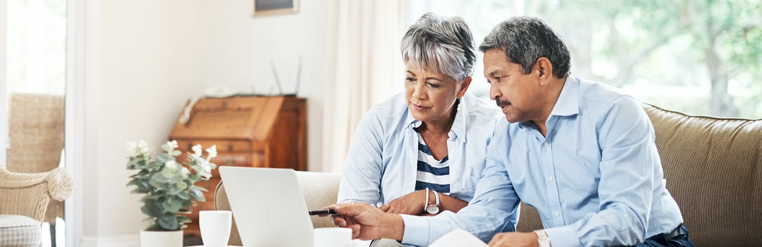 Older couple sits together on the couch looking at a laptop.