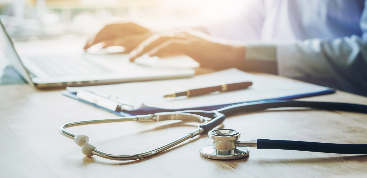 A stethoscope, pen, clipboard and laptop lie on a desk