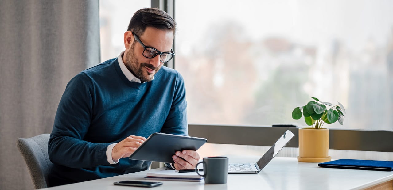 Man with glasses reading his tablet in an office. 