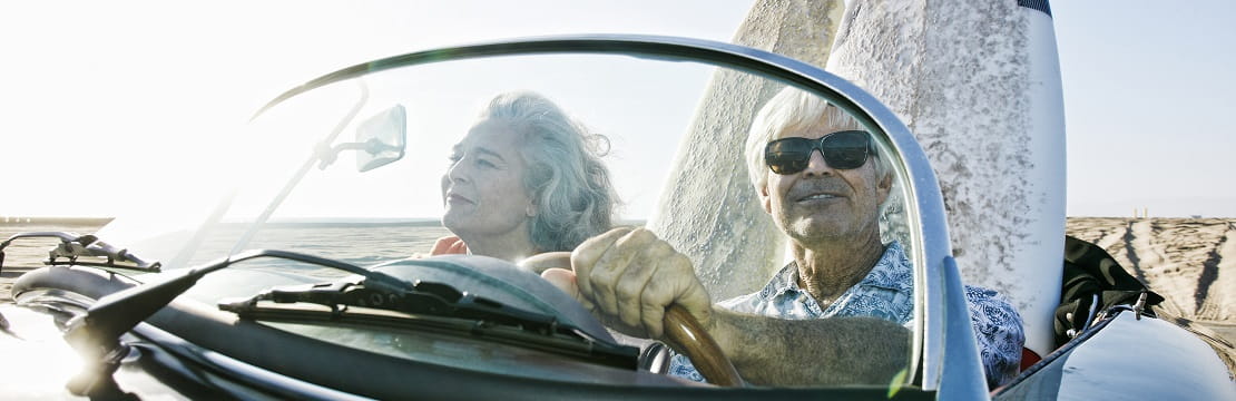 Senior couple driving a car with surfboards in the backseat.