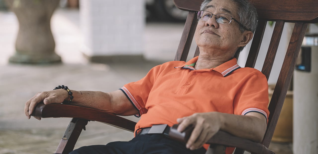 Elderly Asian man sits on a porch. 