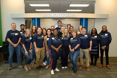 A group of around 20 Raymond James volunteers pose at Finance Park wearing Raymond James Cares shirts