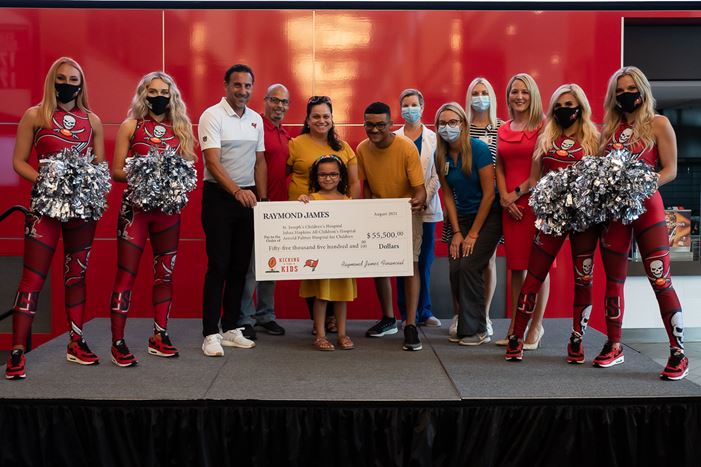 A Kicking for Kids family and Raymond James representative pose with former Bucs kick Martin Gramatica, Bucs cheerleaders and a symbolic check